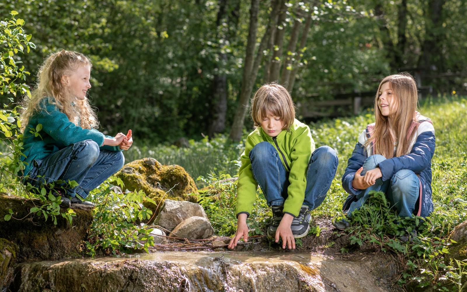 Three children at a creek playing with rocks