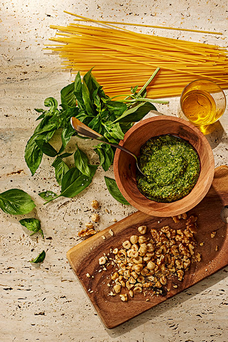 Eine Holzschale mit Pesto und daneben einige Basilikumblätter