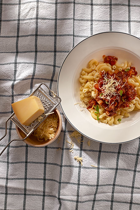 Ein Teller mit Teigwaren und daneben ein Stückkäse auf einer Raffel