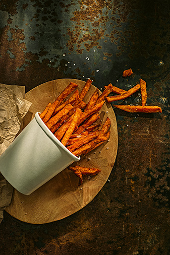 Ein gekippter Behälter mit orangen Süsskartoffel Pommes Frites