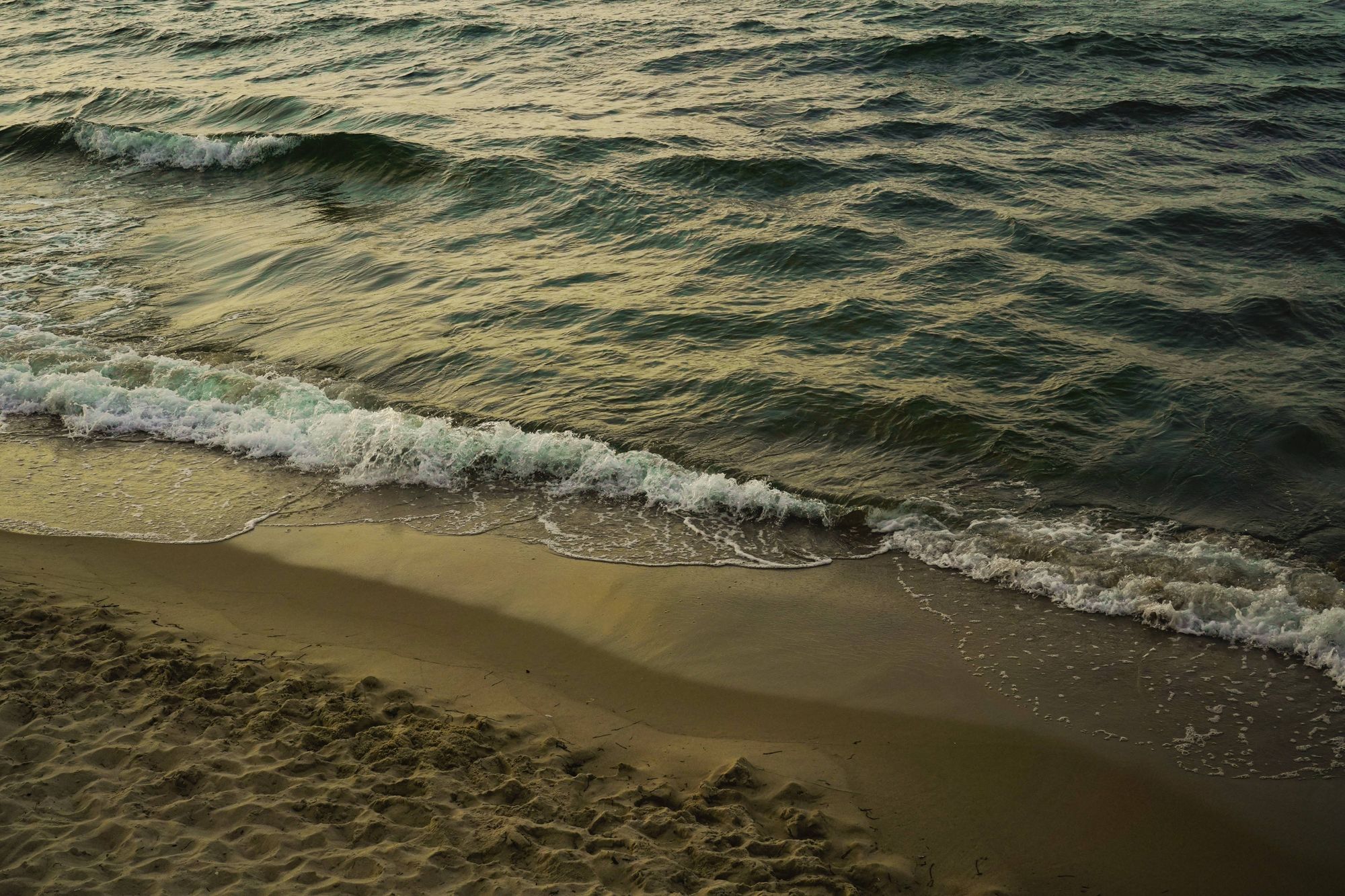 Waves braking on a sand beach, while it gets dark and the sun sets