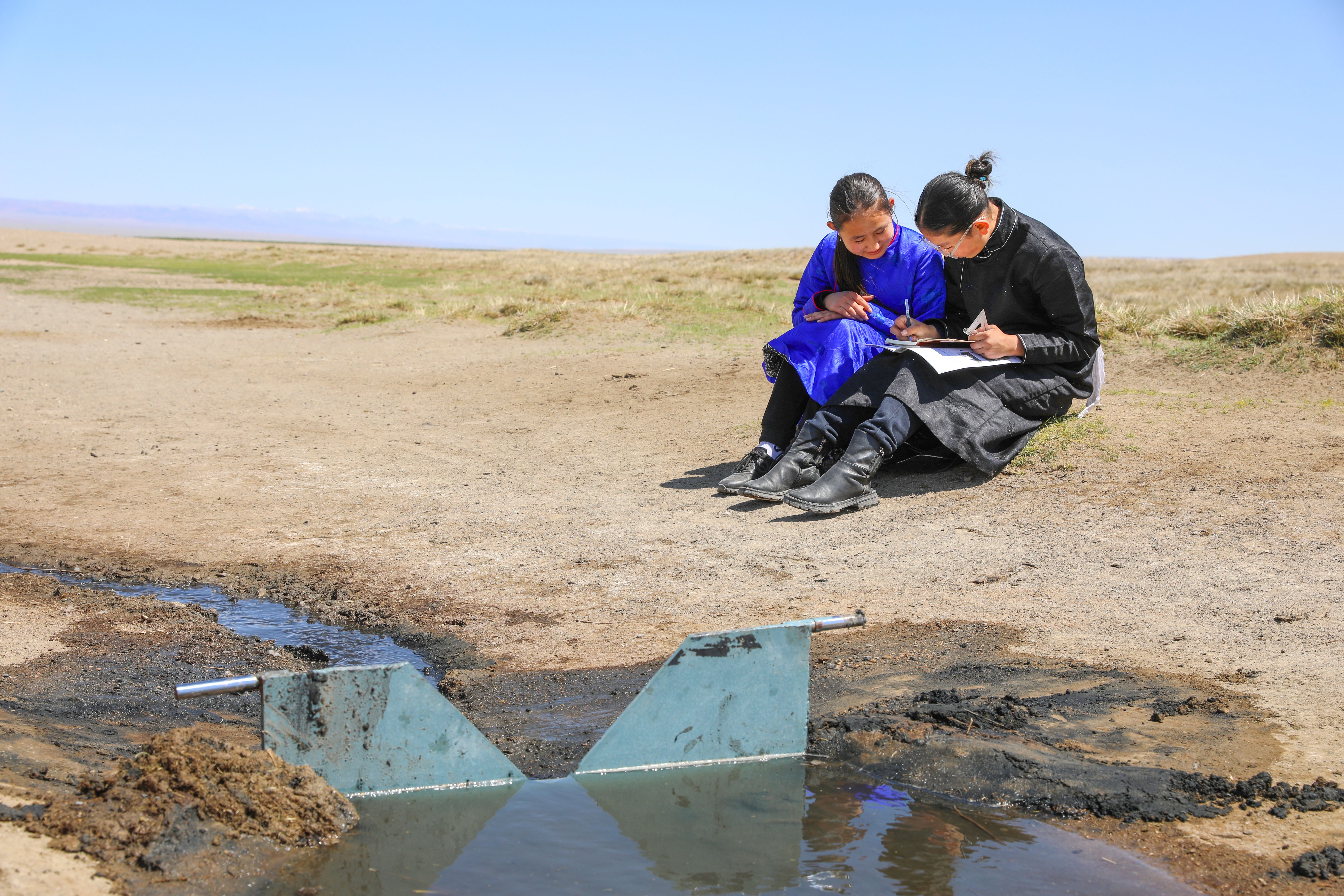 Zwei Mädchen sitzen neben einer Abfluss-Messstation in der Mongolei