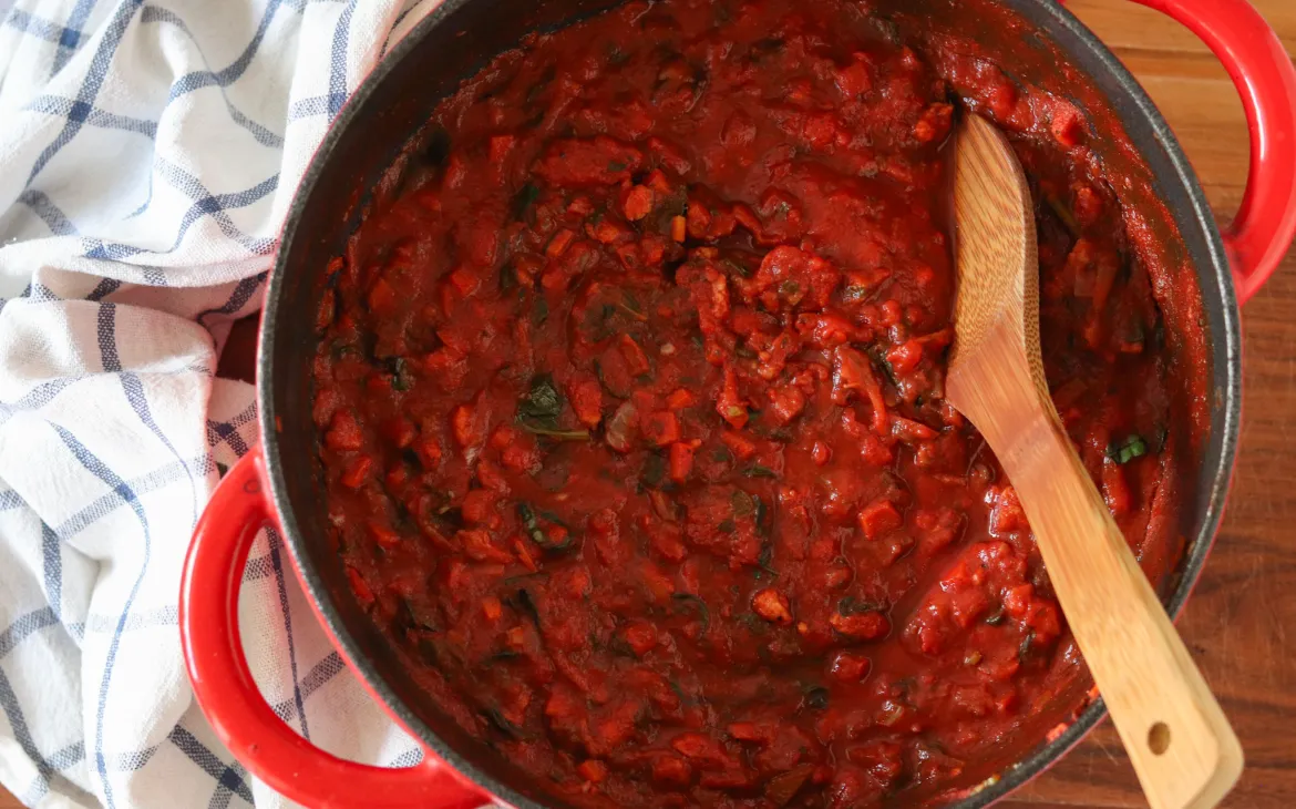 Red pot with vegan bolognese inside and a towel beside