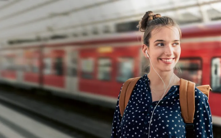 Frau steht lächelnd am Bahnhof 