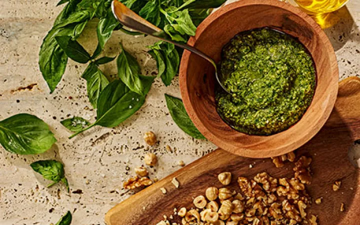 Eine Holzschale mit Pesto und daneben einige Basilikumblätter