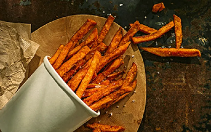 Ein gekippter Behälter mit orangen Süsskartoffel Pommes Frites