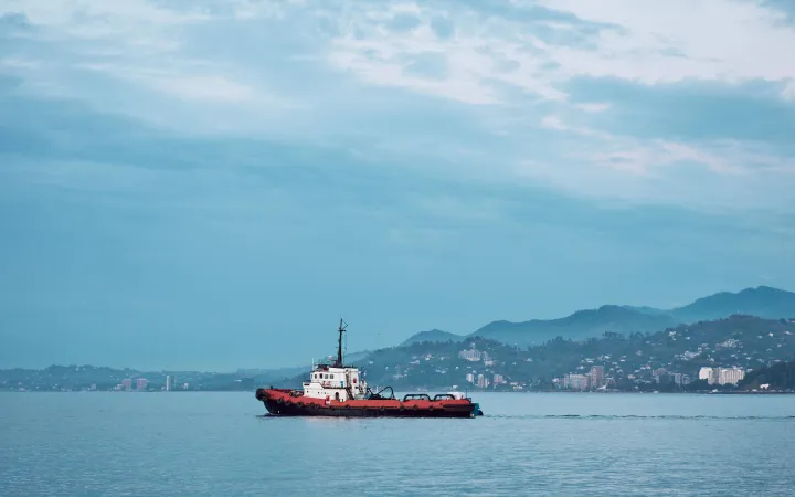 Ein Fischerboot auf stillem Wasser mit Hügeln und Häusern im Hintergrund