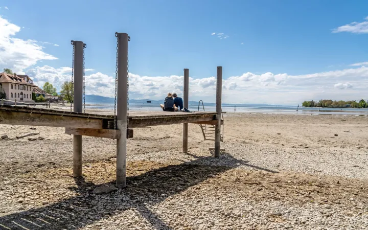 two people sitting on a jetty at lake constance with no water at the shores