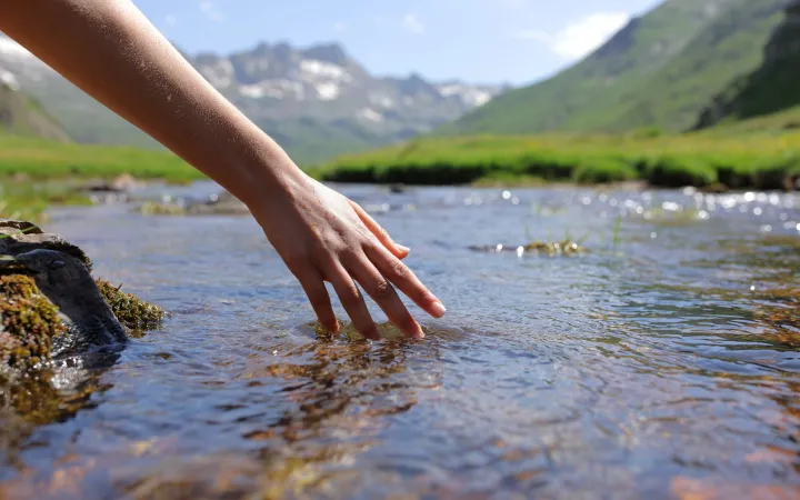 Mountain scene with a clear river and hand touching the water