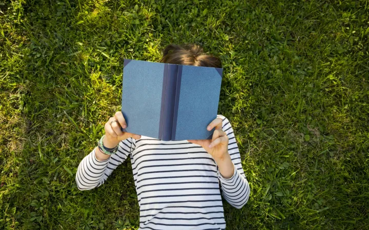 Girl lying on meadow reading a book