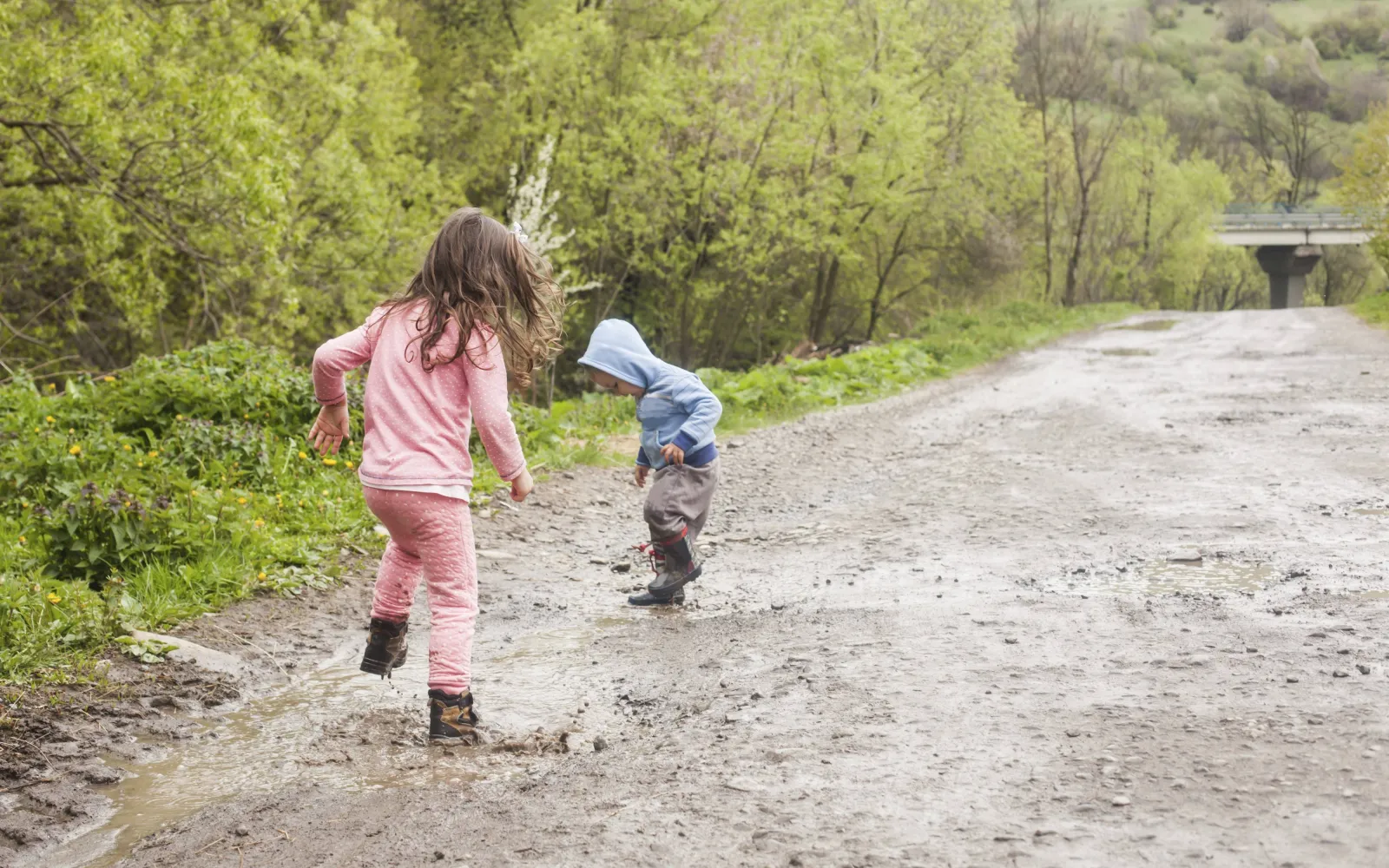 Zwei Kinder spielen in Gummistiefeln im Matsch