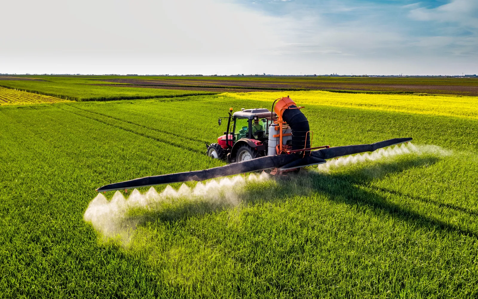Roter Traktor fährt über ein Feld und sprüht mit breiten Armen Pestizide