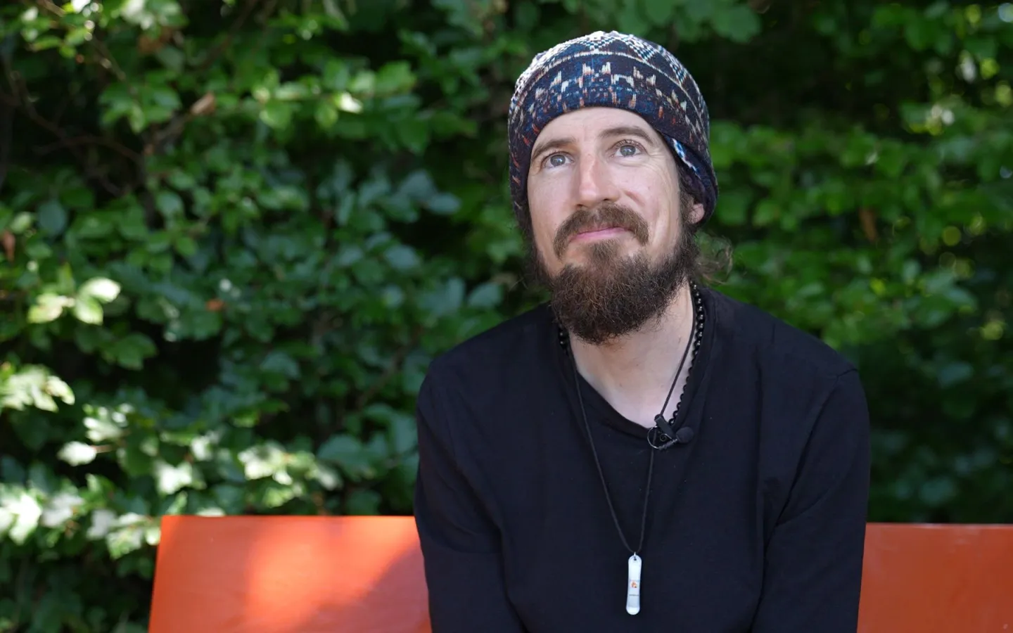 Portrait von Lukas Wullschleger auf oranger Bank mit grünen Blättern im Hintergrund