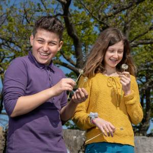 Three teenagers in nature laughing and blowing dandelions