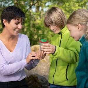 A teacher with two students in nature looking at a newt with a cup magnifier