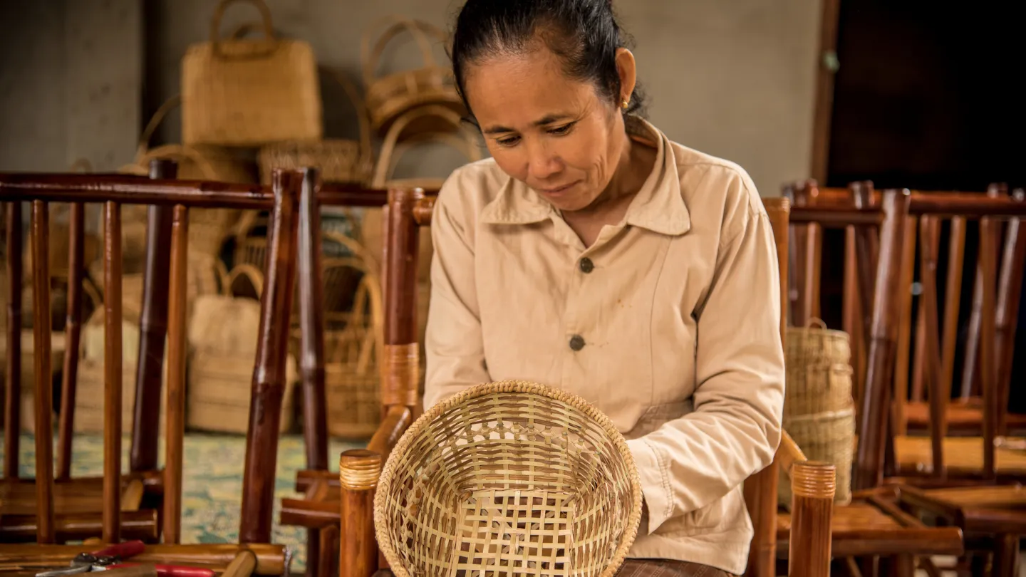 Eine Frau flicht einen Rattan-Korb in Laos