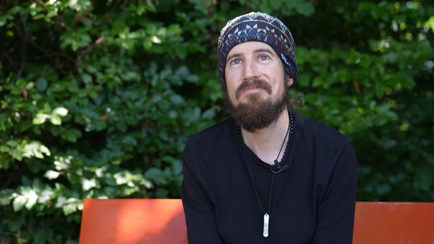 Portrait von Lukas Wullschleger auf oranger Bank mit grünen Blättern im Hintergrund