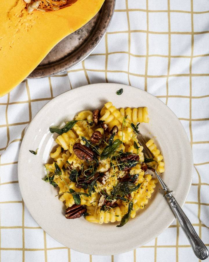 Teller mit Pasta und Kürbis auf kariertem Tischtuch